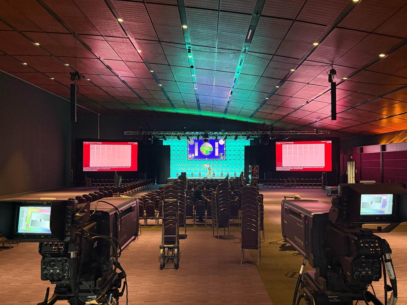 Conference general session with center LED, two flanking screens and broadcast cameras on tripods