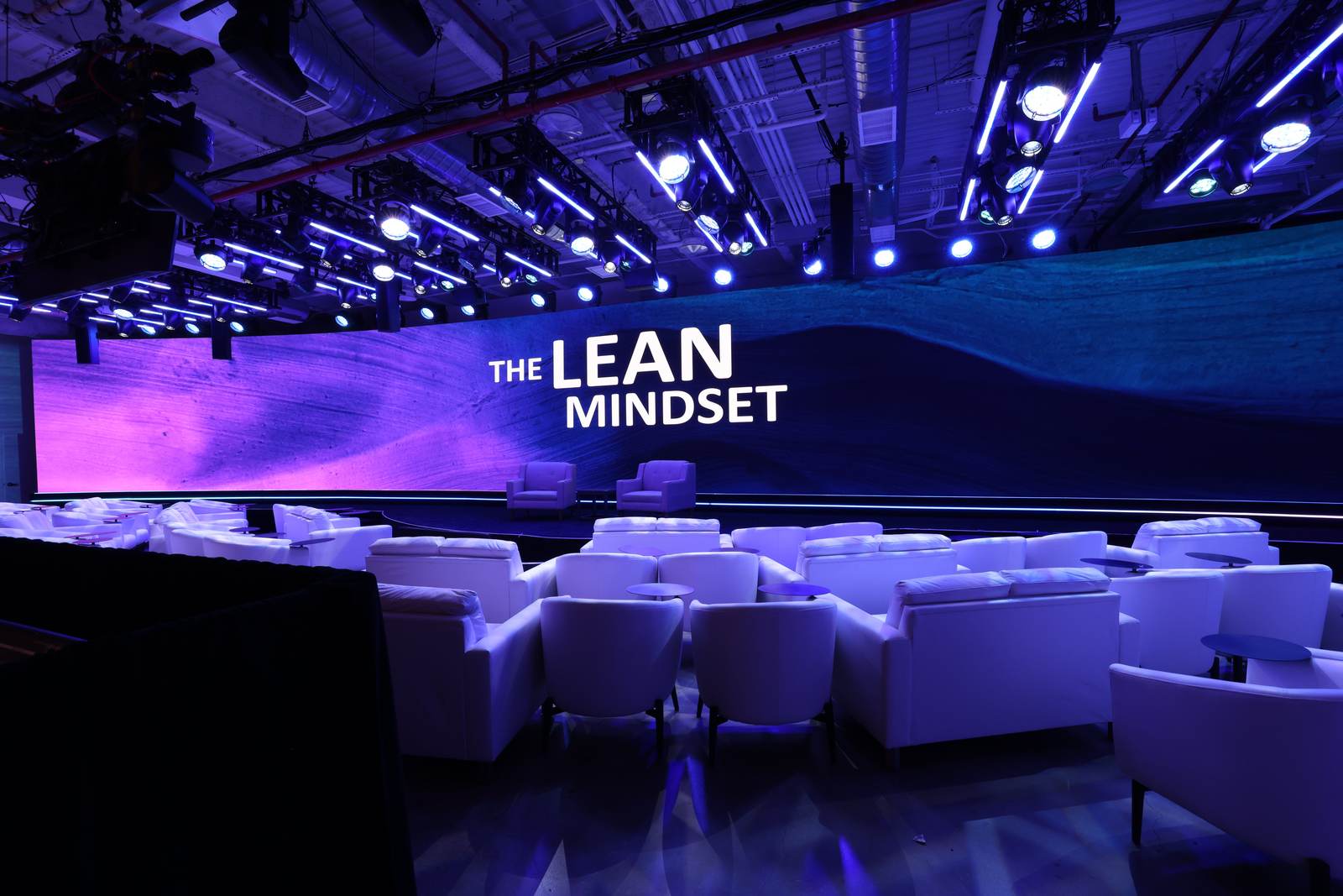 Curved LED wall with white lounge seating and a dense lighting rig